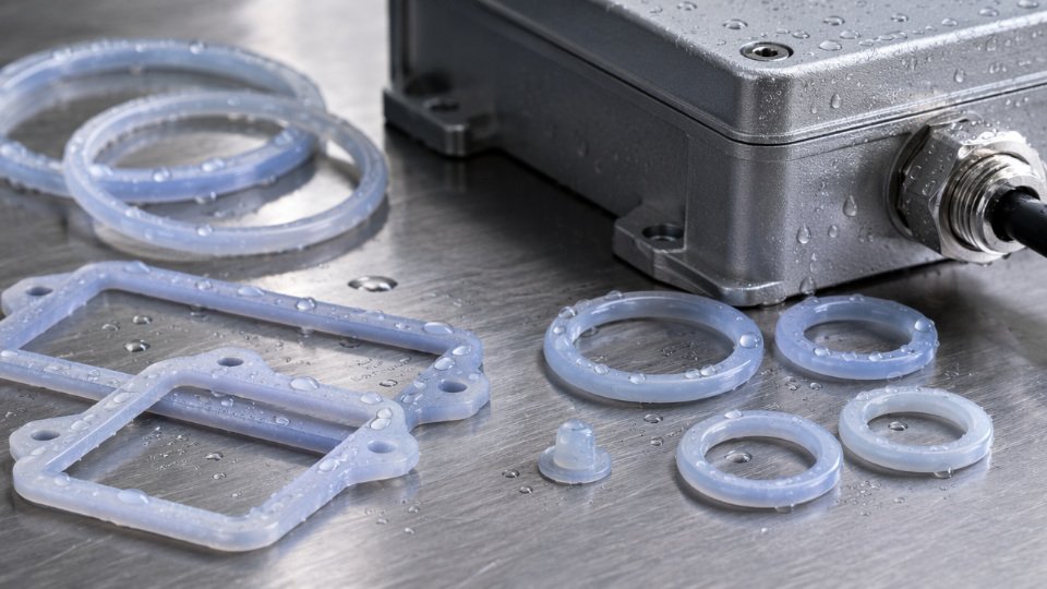 LSR gasket and O-ring components arranged next to an IP68-rated industrial enclosure with water droplets beading on the silicone surface