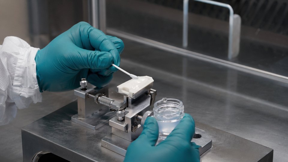Technician applying HF gel to a ceramic surface in an industrial setting before silane treatment
