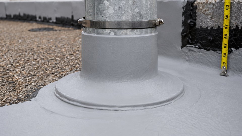 Close-up of a seamless liquid rubber membrane wrapping continuously from a flat roof field coat up and around a metal pipe boot penetration with no laps or seams
