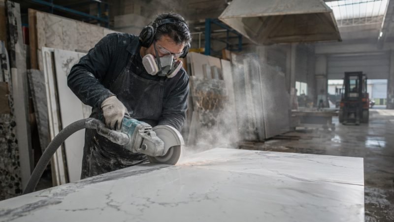 Industrial stone fabricator cutting engineered quartz countertop in a dusty workshop environment
